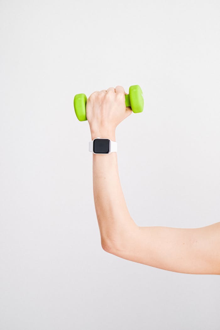 Arm holding a green dumbbell with a smartwatch on wrist against a white background.